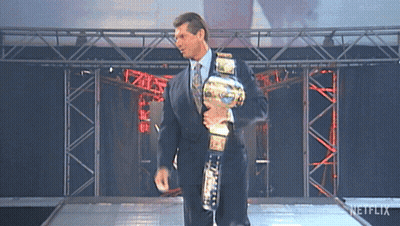 A Man In A Suit And Tie Is Holding A Wrestling Championship Belt GIF