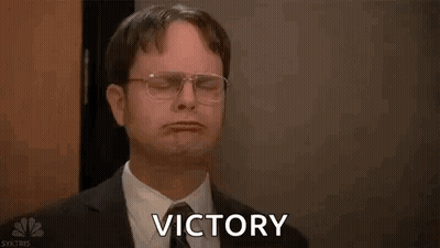 A Man In A Suit And Tie Is Holding His Arms In The Air And Saying Victory . GIF