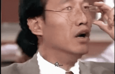 A Man In A Suit And Tie Is Holding His Glasses Up To His Eyes . GIF