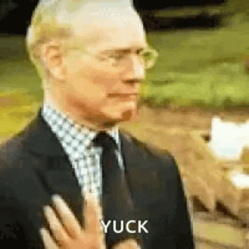 A Man In A Suit And Tie Is Holding His Hand To His Chest And Says Yuck . GIF