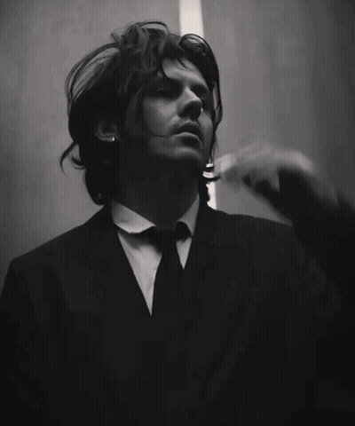 A Man In A Suit And Tie Is Holding His Hand To His Head GIF