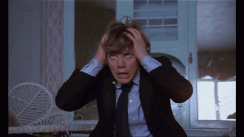 A Man In A Suit And Tie Is Holding His Head In Pain GIF