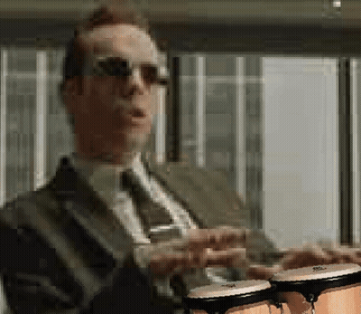 A Man In A Suit And Tie Is Holding Two Bongos In His Hands GIF