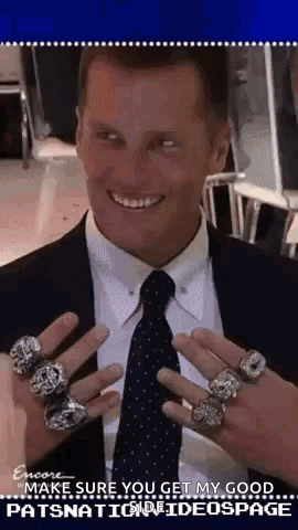 A Man In A Suit And Tie Is Holding Up A Bunch Of Rings On His Fingers . GIF
