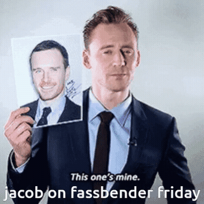 A Man In A Suit And Tie Is Holding Up A Picture Of Jacob On Fassbender Friday GIF