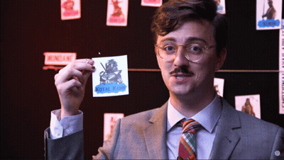A Man In A Suit And Tie Is Holding Up A Sticker That Says Kotal Karim GIF
