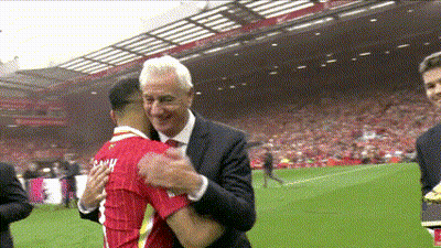 A Man In A Suit And Tie Is Hugging A Man In A Red Shirt On A Soccer Field GIF