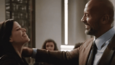 A Man In A Suit And Tie Is Hugging A Woman In A Room And Smiling . GIF