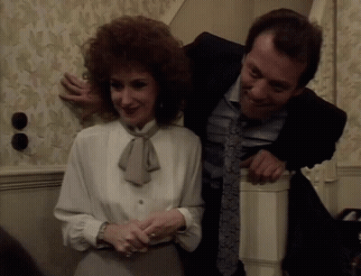 A Man In A Suit And Tie Is Hugging A Woman In A White Blouse GIF