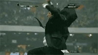 A Man In A Suit And Tie Is Jumping In The Air While Watching A Soccer Game . GIF