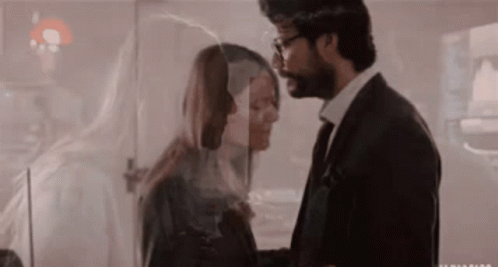 A Man In A Suit And Tie Is Kissing A Woman Behind A Glass . GIF