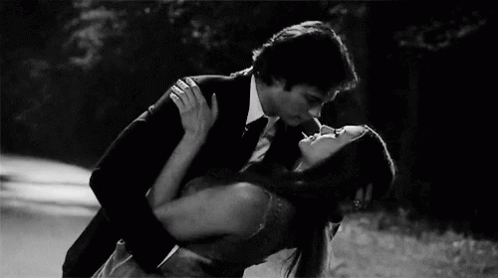 A Man In A Suit And Tie Is Kissing A Woman In A Dress . GIF