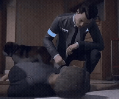A Man In A Suit And Tie Is Kneeling Down Next To Another Man Laying On The Floor . GIF