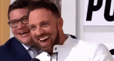 A Man In A Suit And Tie Is Laughing Next To Another Man In A White Jacket . GIF