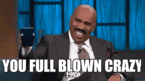 A Man In A Suit And Tie Is Laughing While Holding A Cell Phone And Saying `` You Full Blown Crazy '' . GIF