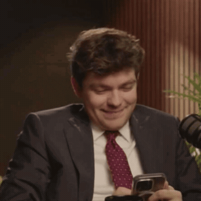A Man In A Suit And Tie Is Laughing While Holding A Phone GIF