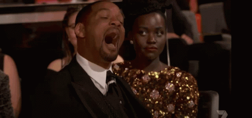 A Man In A Suit And Tie Is Laughing While Sitting Next To A Woman GIF