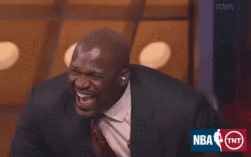 A Man In A Suit And Tie Is Laughing While Sitting On A Stage . GIF