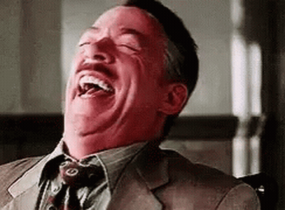 A Man In A Suit And Tie Is Laughing With His Eyes Closed And His Mouth Open . GIF