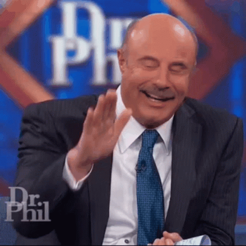 A Man In A Suit And Tie Is Laughing With His Eyes Closed In Front Of A Dr Phil Logo GIF