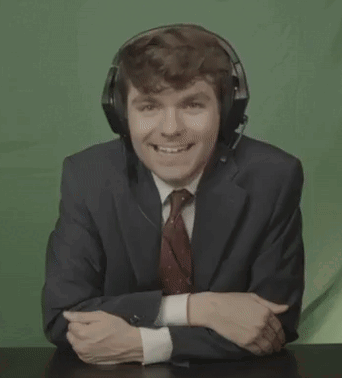 A Man In A Suit And Tie Is Laughing With His Mouth Open While Wearing Headphones . GIF