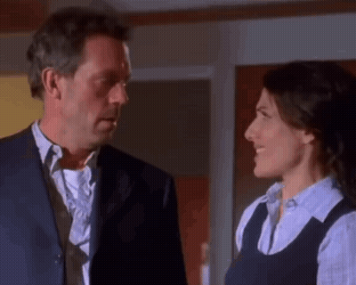 A Man In A Suit And Tie Is Looking At A Woman In A Blue Shirt . GIF
