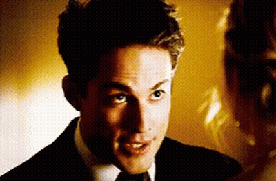 A Man In A Suit And Tie Is Looking At A Woman In A Dress GIF