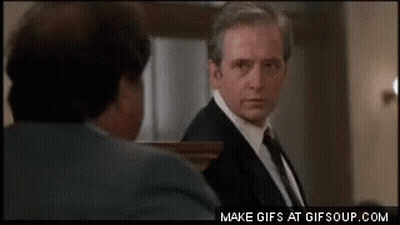 A Man In A Suit And Tie Is Looking At Another Man In A Suit And Tie . GIF