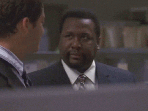 A Man In A Suit And Tie Is Looking At Another Man GIF