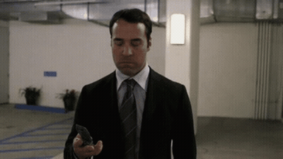 A Man In A Suit And Tie Is Looking At His Cell Phone . GIF