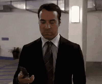 A Man In A Suit And Tie Is Looking At His Cell Phone . GIF
