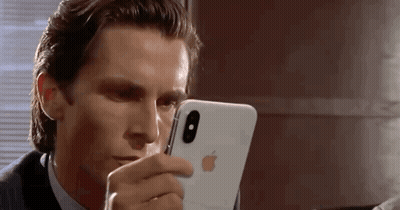 A Man In A Suit And Tie Is Looking At His Iphone . GIF