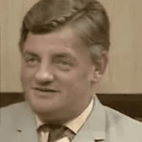 A Man In A Suit And Tie Is Looking At The Camera And Smiling . GIF