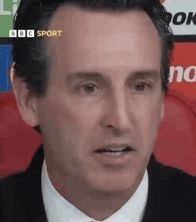 A Man In A Suit And Tie Is Looking At The Camera While Sitting In A Chair . GIF