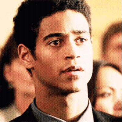 A Man In A Suit And Tie Is Looking At The Camera With A Group Of People In The Background . GIF