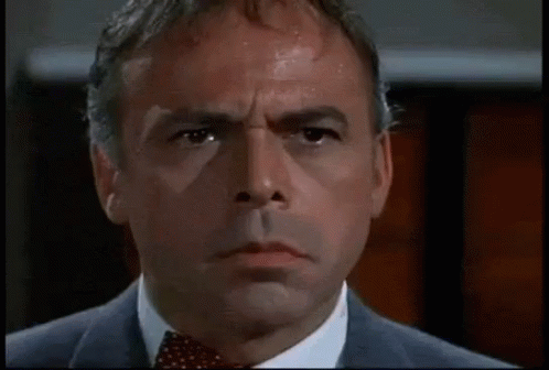 A Man In A Suit And Tie Is Looking At The Camera With A Serious Look On His Face . GIF