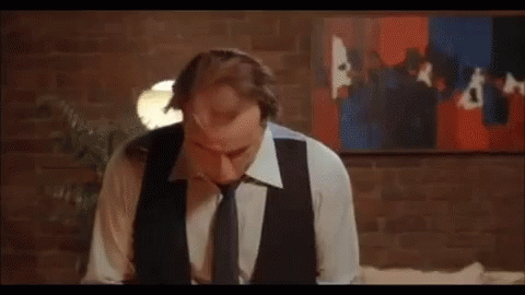 A Man In A Suit And Tie Is Looking Down At Something . GIF