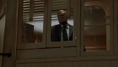 A Man In A Suit And Tie Is Looking Out A Window GIF
