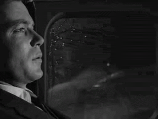 A Man In A Suit And Tie Is Looking Out Of A Window . GIF