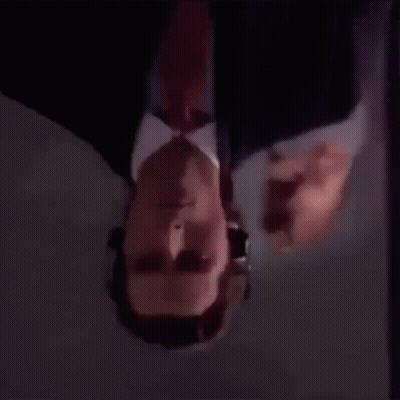 A Man In A Suit And Tie Is Looking Upside Down . GIF