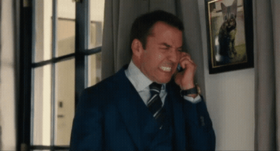 A Man In A Suit And Tie Is Making A Face While Talking On A Cell Phone GIF