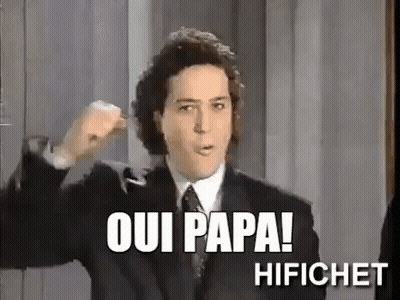 A Man In A Suit And Tie Is Making A Fist In The Air And Says Oui Papa ! GIF