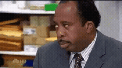 A Man In A Suit And Tie Is Making A Funny Face In Front Of A Shelf Of Envelopes . GIF