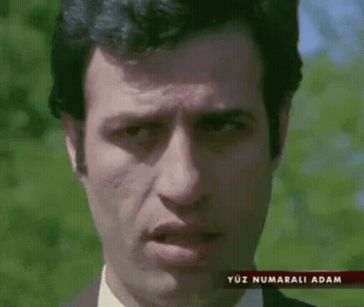 A Man In A Suit And Tie Is Making A Funny Face In Front Of Trees . GIF