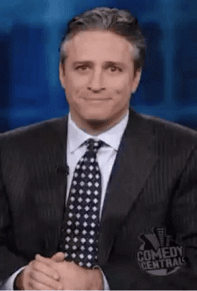 A Man In A Suit And Tie Is Making A Funny Face While Giving A Thumbs Up . GIF