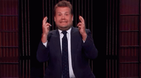 A Man In A Suit And Tie Is Making A Funny Face While Holding His Fingers Crossed . GIF
