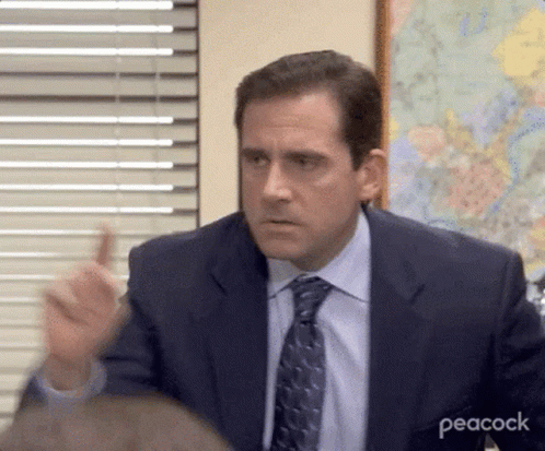 A Man In A Suit And Tie Is Making A Funny Face While Sitting At A Table . GIF