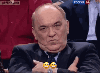 A Man In A Suit And Tie Is Making A Funny Face While Sitting In A Audience . GIF
