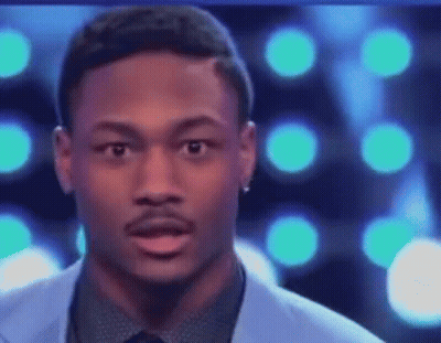 A Man In A Suit And Tie Is Making A Funny Face While Standing In Front Of A Blue Background . GIF