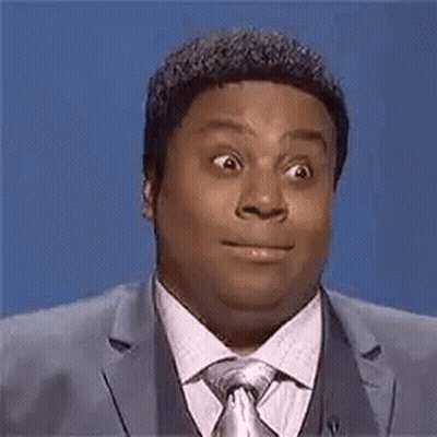 A Man In A Suit And Tie Is Making A Funny Face While Standing In Front Of A Blue Background . GIF